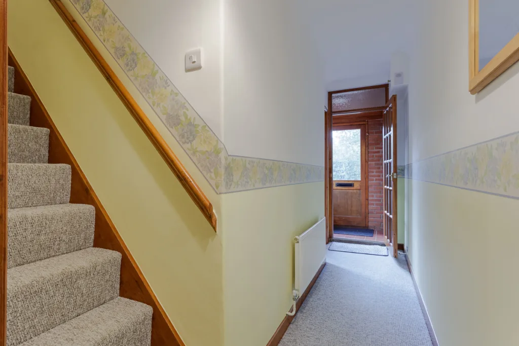 Carpeted hallway with staircase and wooden front door.
