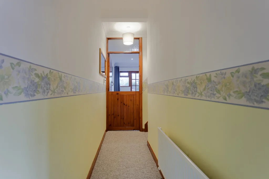 Narrow hallway with floral wallpaper and wooden door.