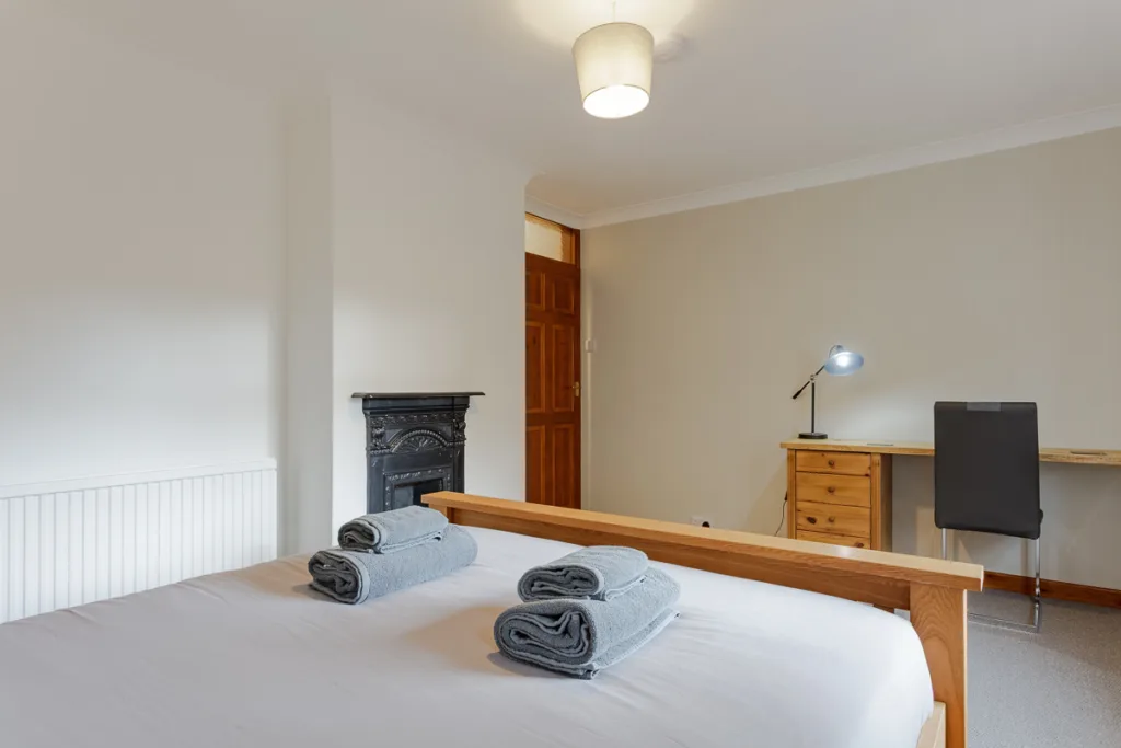 Cosy bedroom with bed, desk, and towels.
