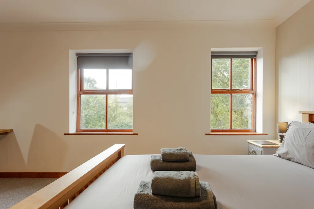 Bright bedroom with windows, bed, and folded towels.