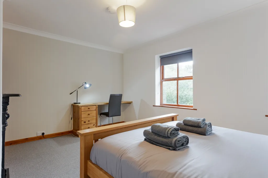 Minimalist bedroom with bed, desk, and window view.