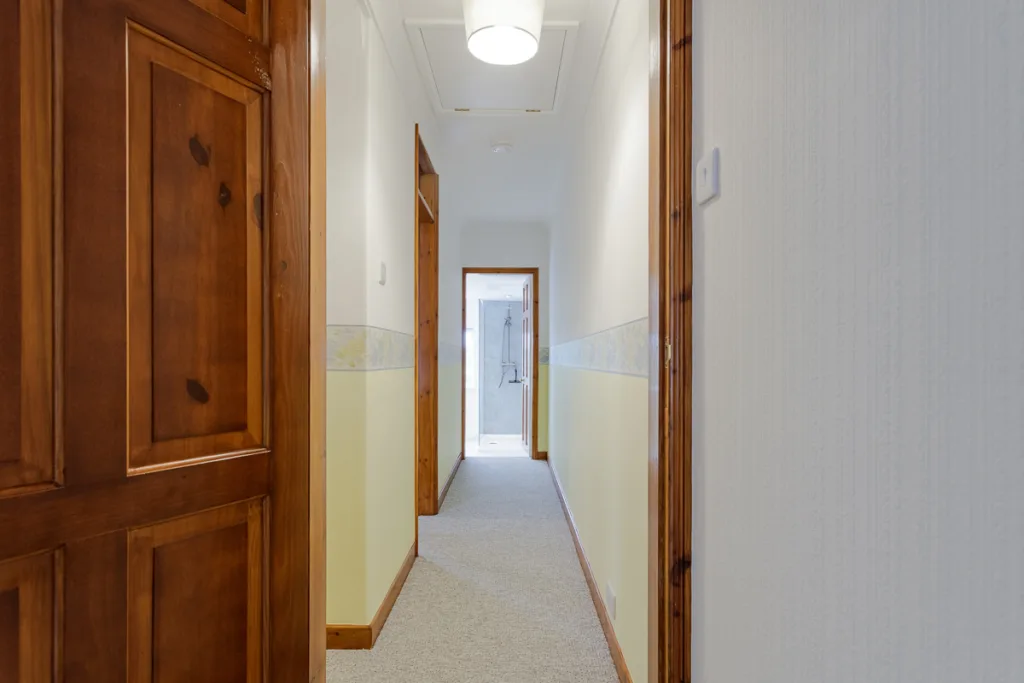 Narrow hallway with wooden doors and light fixture.