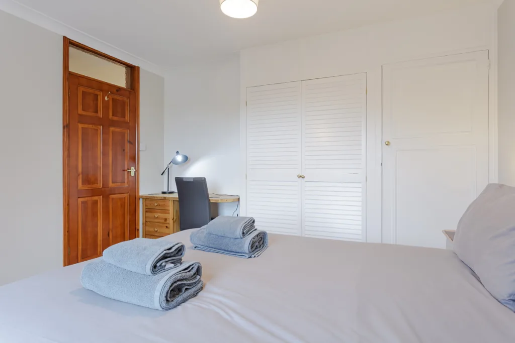 Bright bedroom with desk and towels on bed.