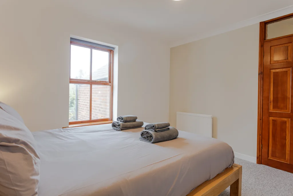 Minimalist bedroom with towels on bed, wooden window.