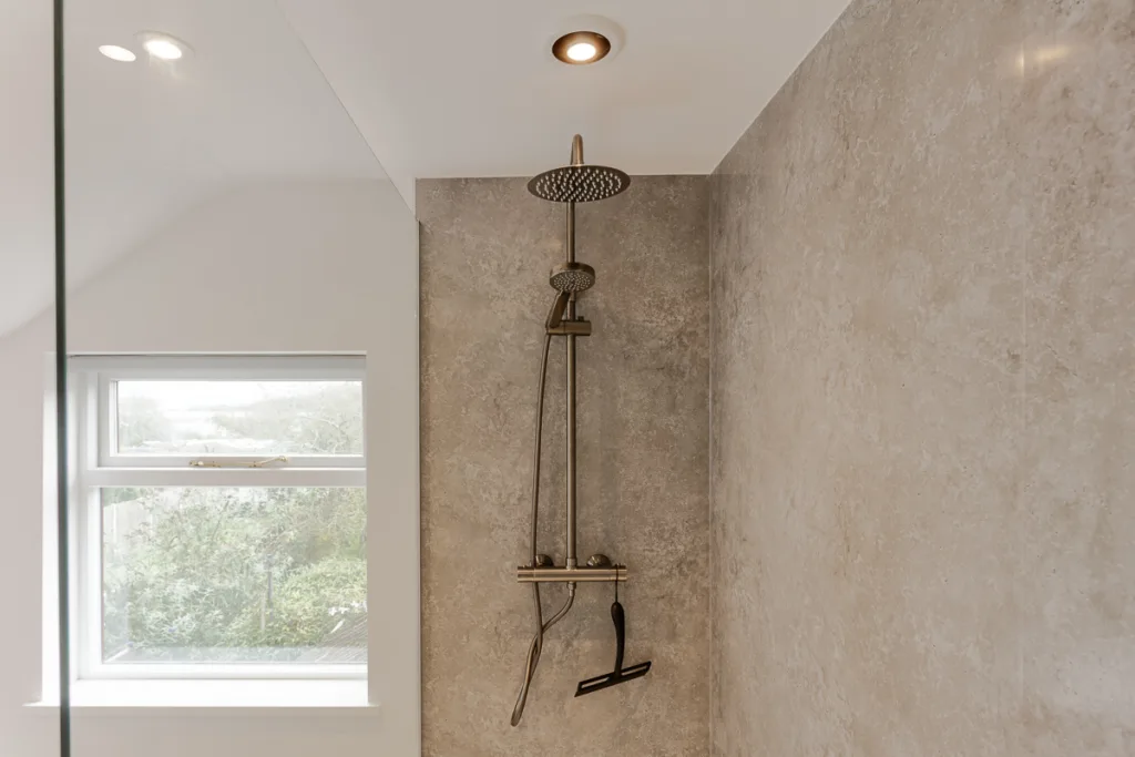 Modern shower with beige stone wall and window view.