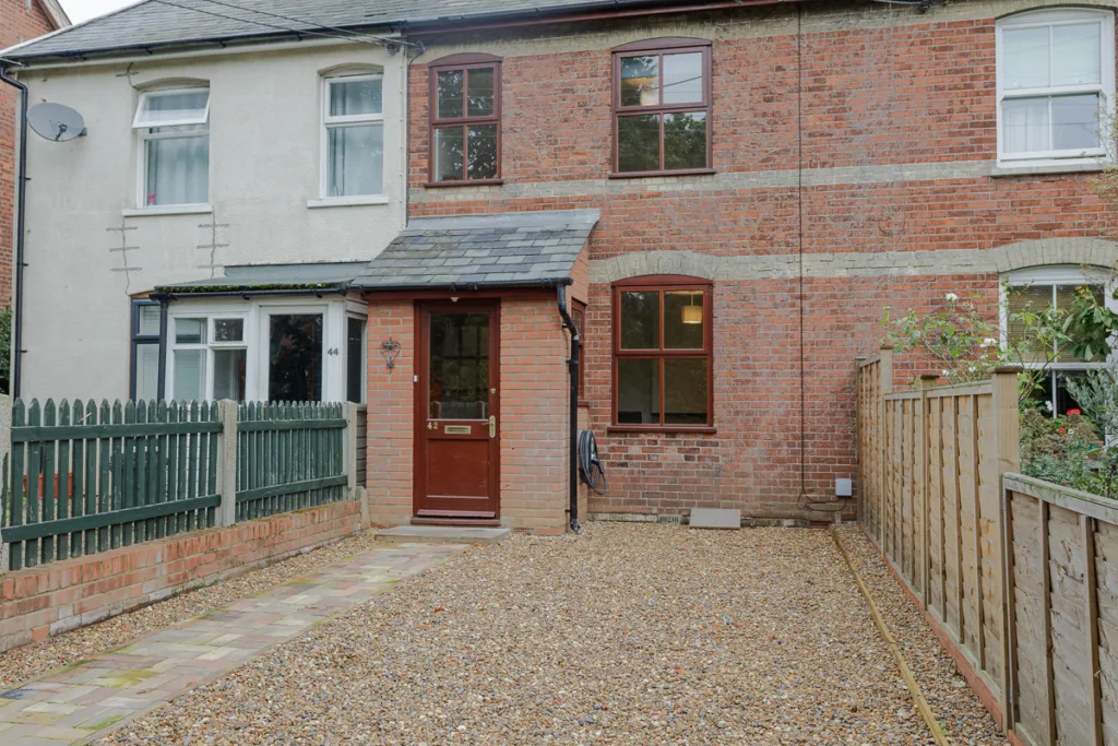 Brick terraced house with gravel driveway and garden fence.