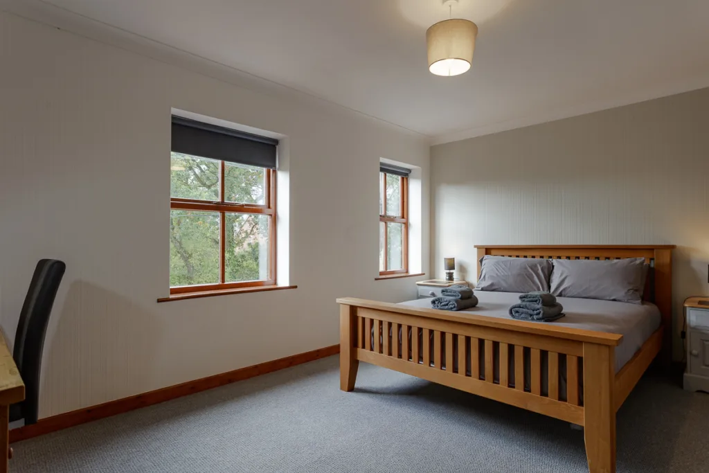 Comfortable bedroom with wooden bed and large windows.