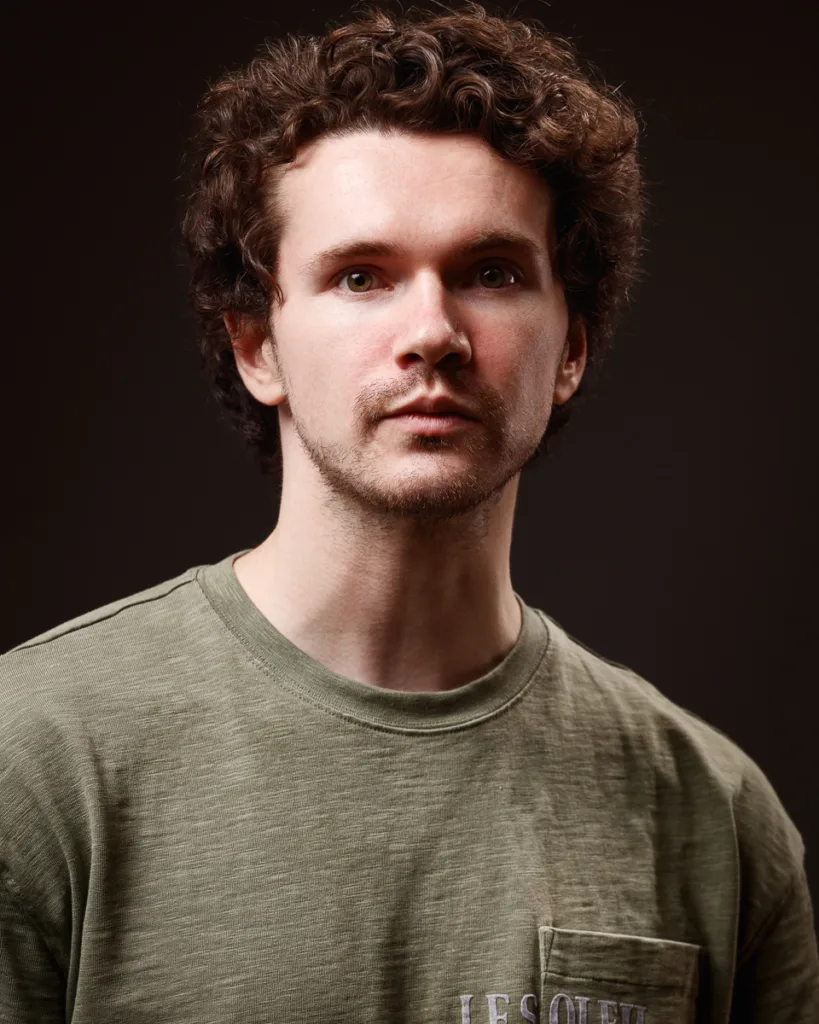 Man in green shirt with curly hair, thoughtful expression.