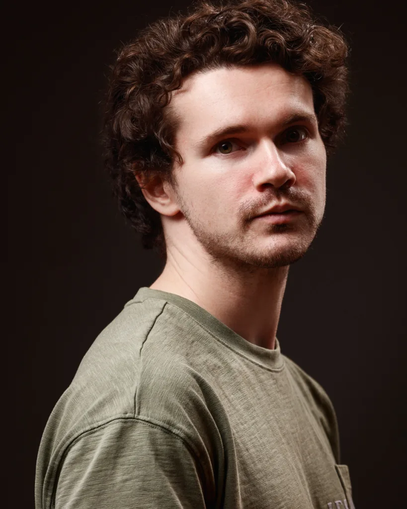 Man in green shirt with curly hair posing.