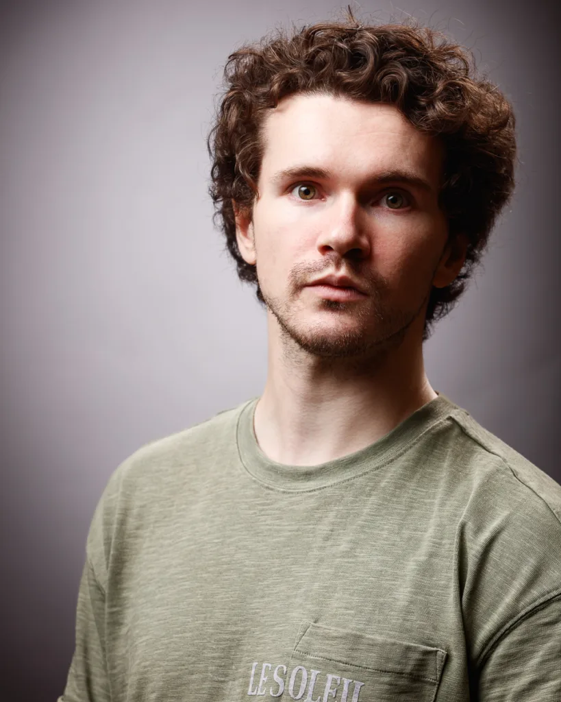 Curly-haired man in green shirt posing.