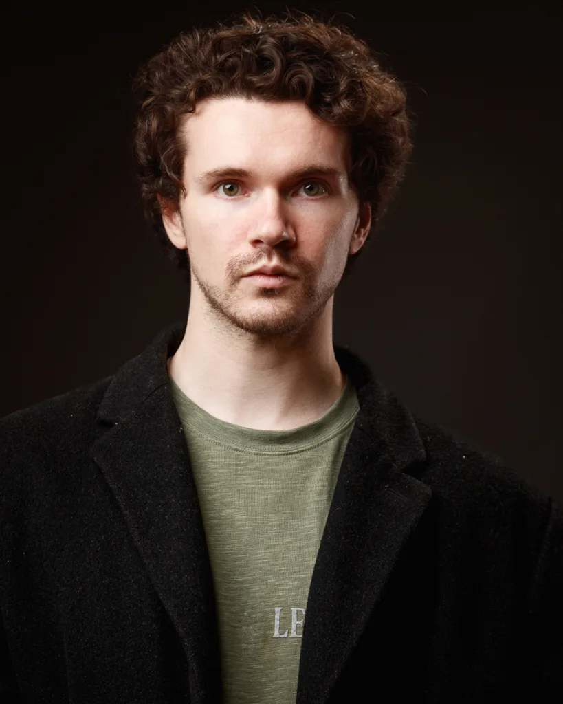 Man in dark coat and green shirt portrait.
