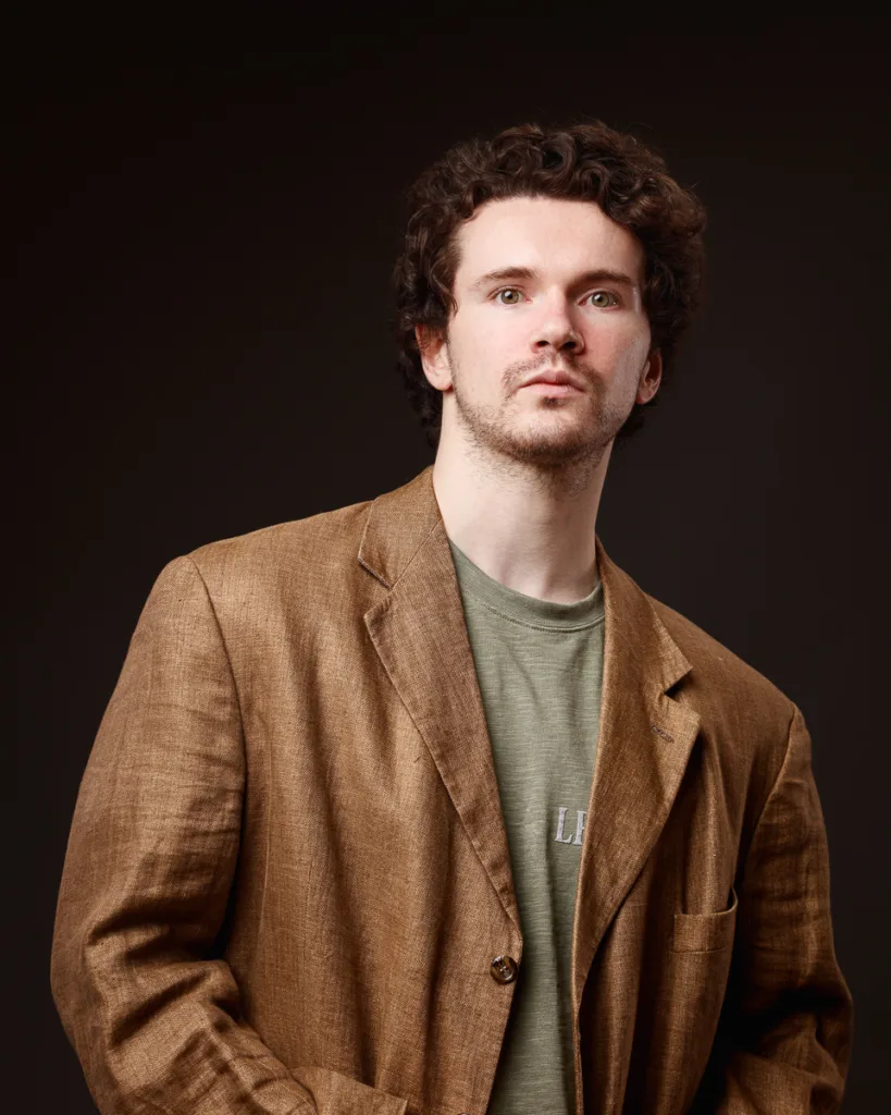 Portrait of man in brown blazer, dark background.