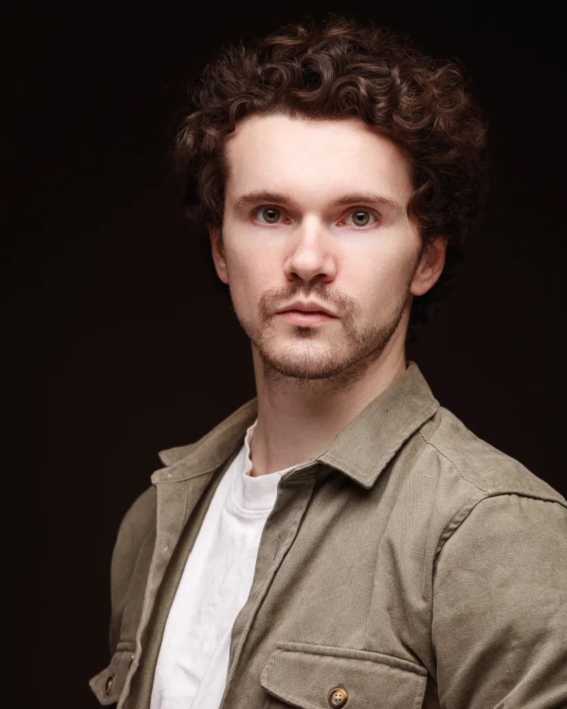 Man with curly hair wearing olive jacket.