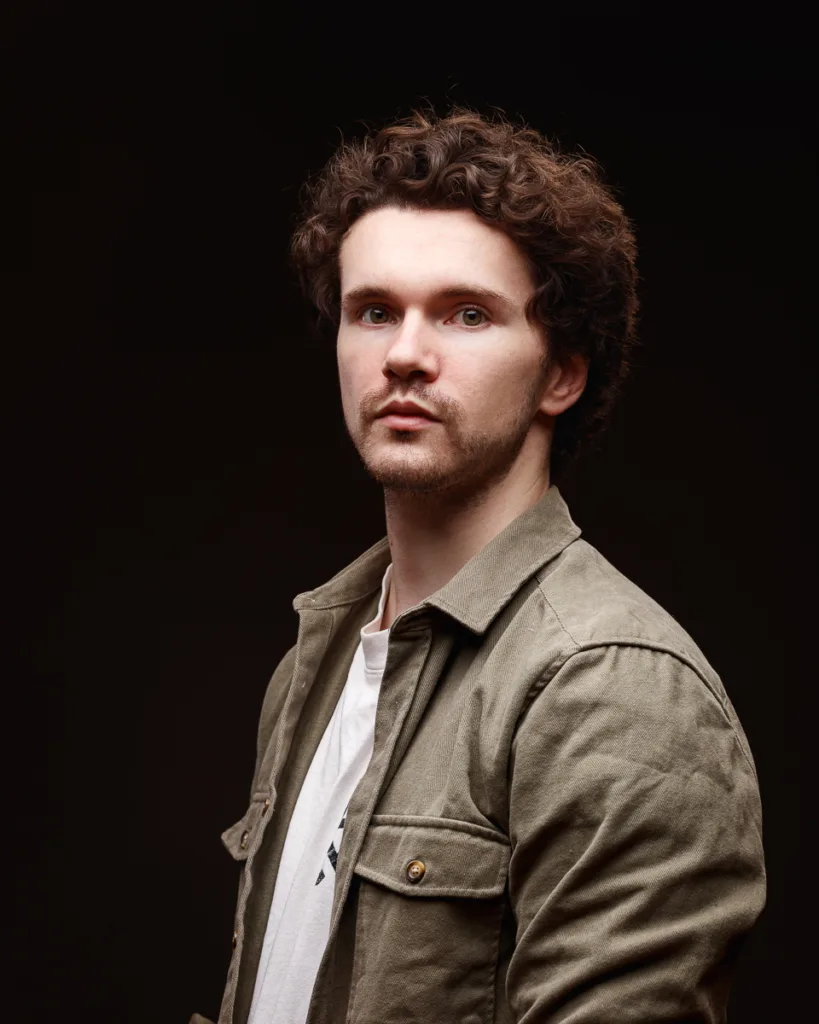 Man wearing green jacket against dark background.