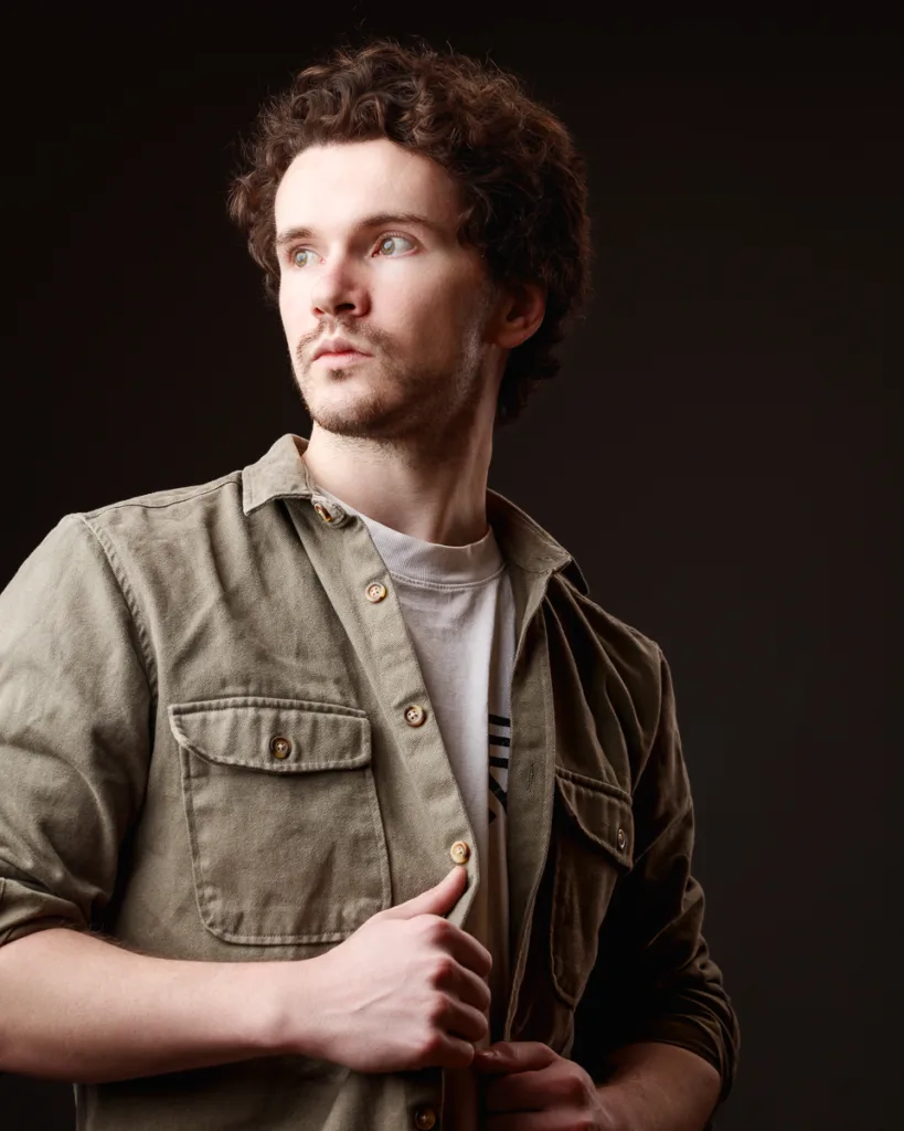 Man in brown jacket looks thoughtful.