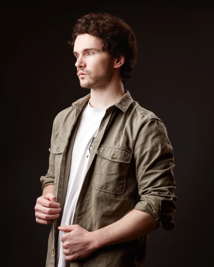 Man in brown shirt looking away, dark background.