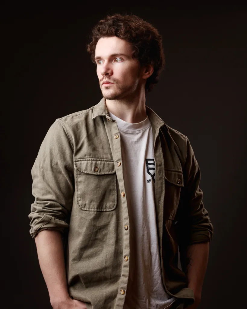 Man in casual shirt looking sideways, dark background.