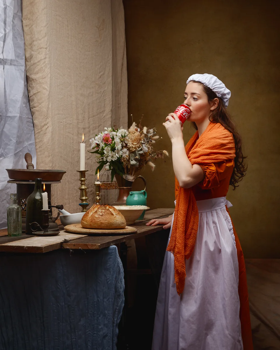 Commercial photograph of a woman in period costume drinking from a can in a candlelit kitchen set