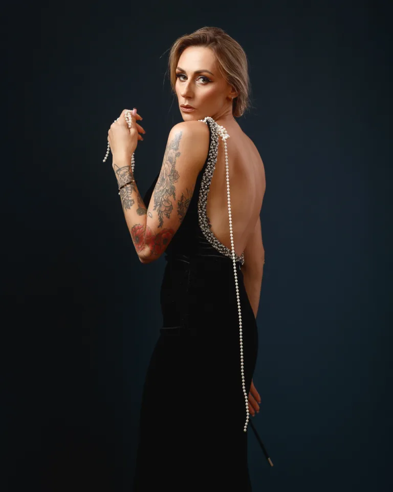Woman in elegant dress with tattoos and pearls.