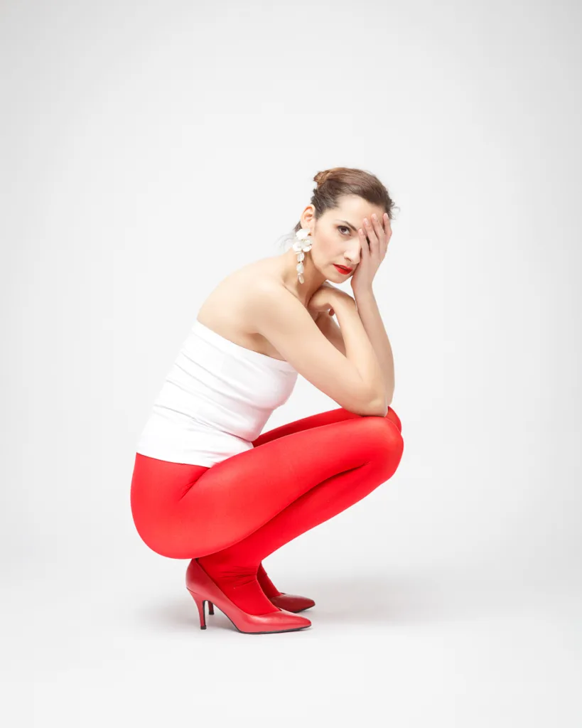 Woman in red tights and heels, thoughtful pose.