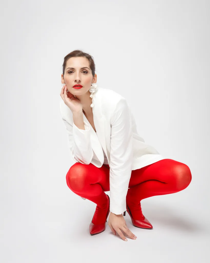 Person in white blazer, red leggings, posing fashionably.