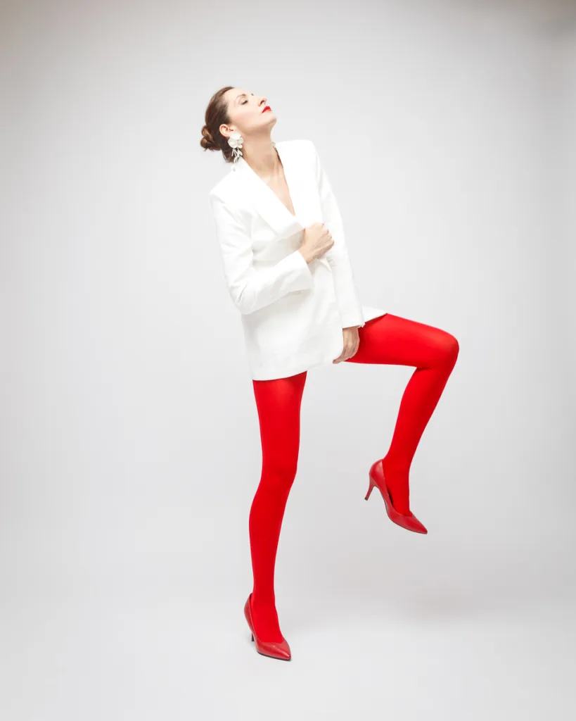Person posing in white blazer and red shoes