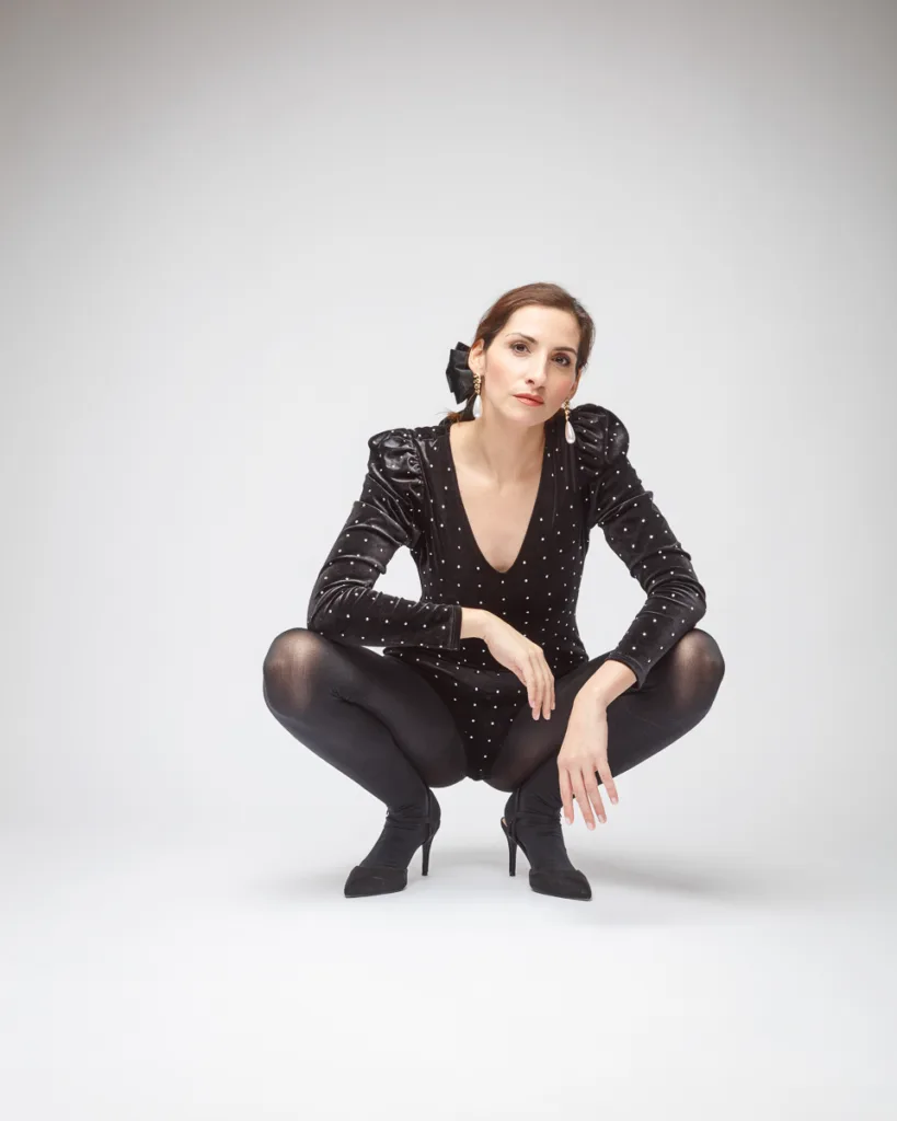 Woman in black outfit crouching on white background.
