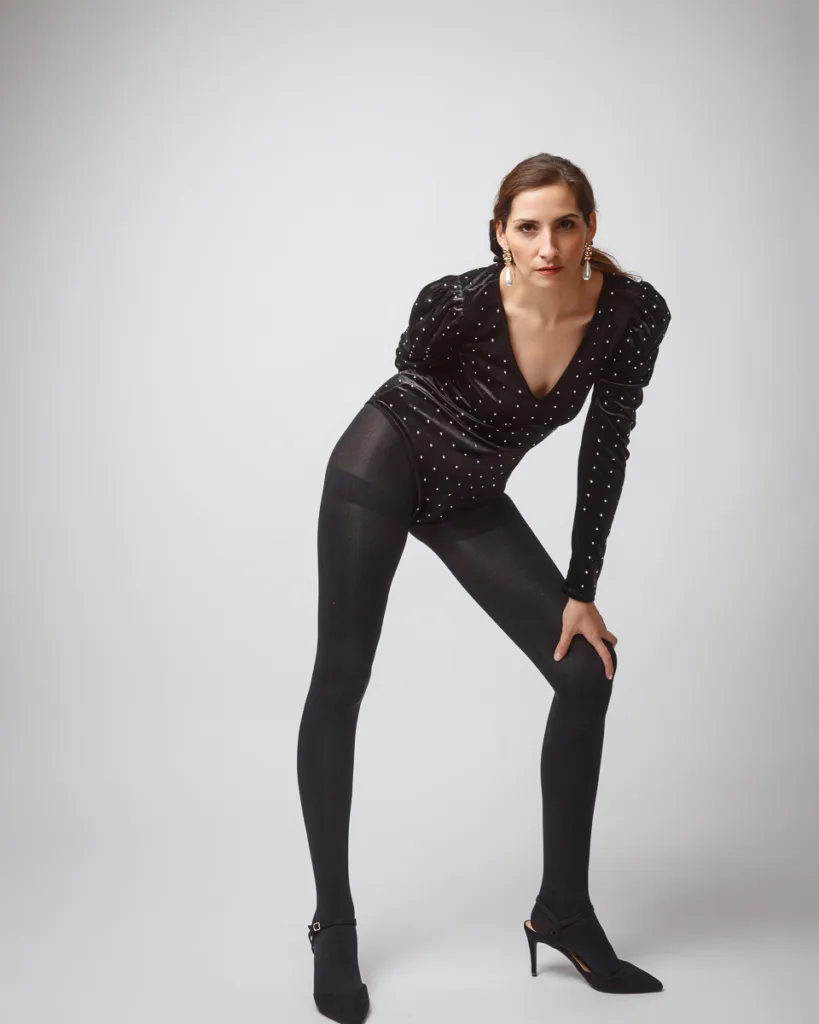 Woman posing in black outfit and heels.