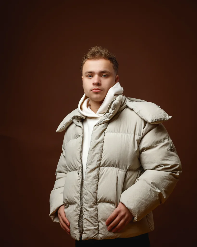 Person wearing beige puffer jacket against brown background.