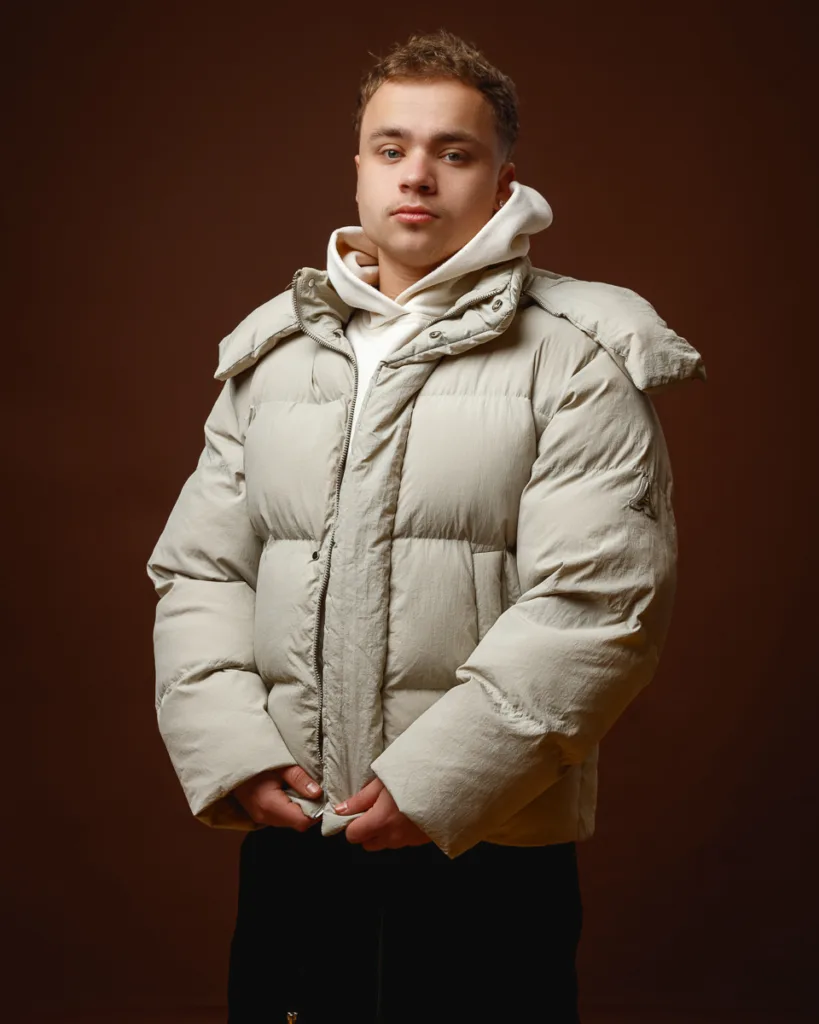 Person wearing beige puffer jacket, brown background.