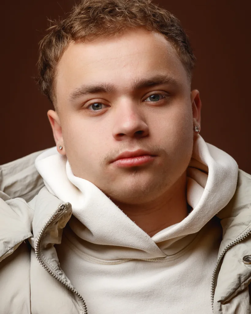 Person in hoodie and jacket, brown background.
