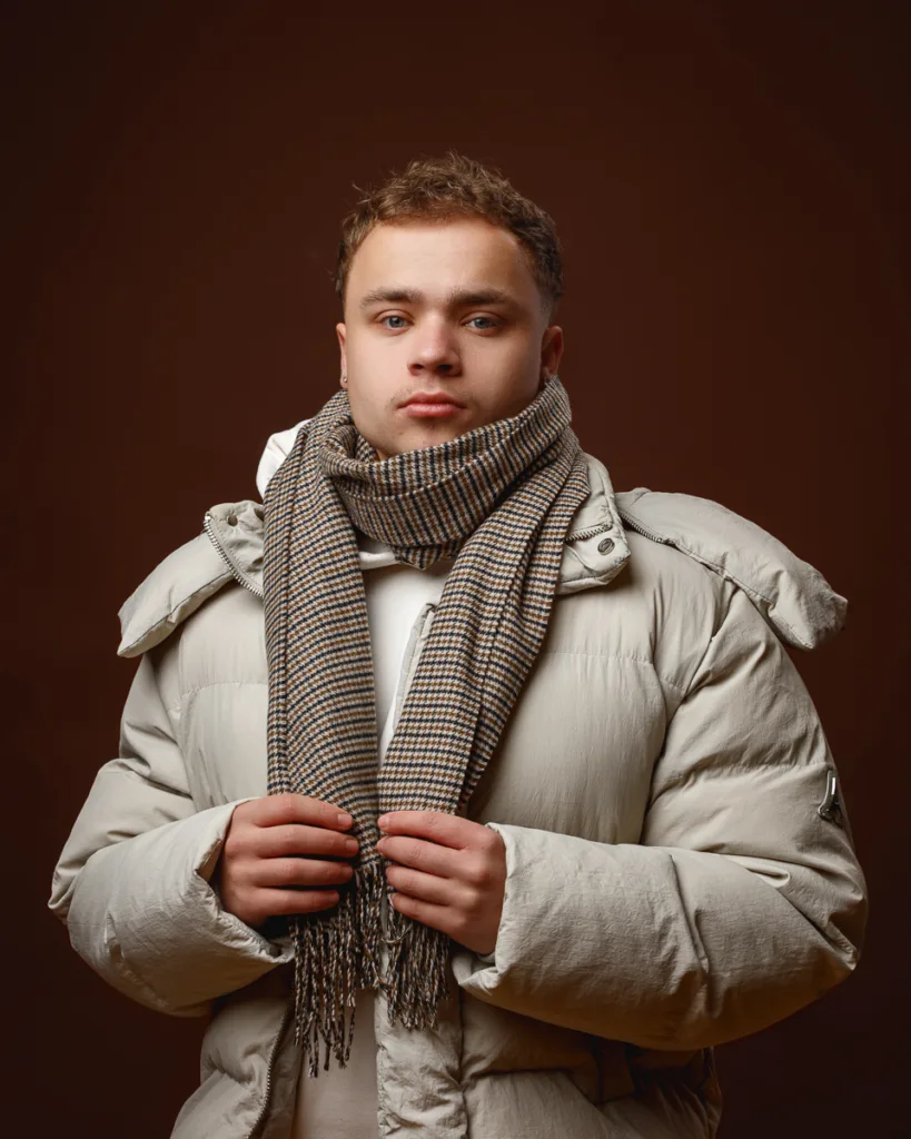 Person in warm coat and scarf, brown background.