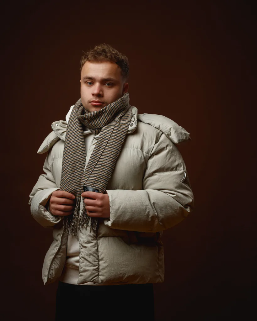 Person in winter coat and scarf, brown background.