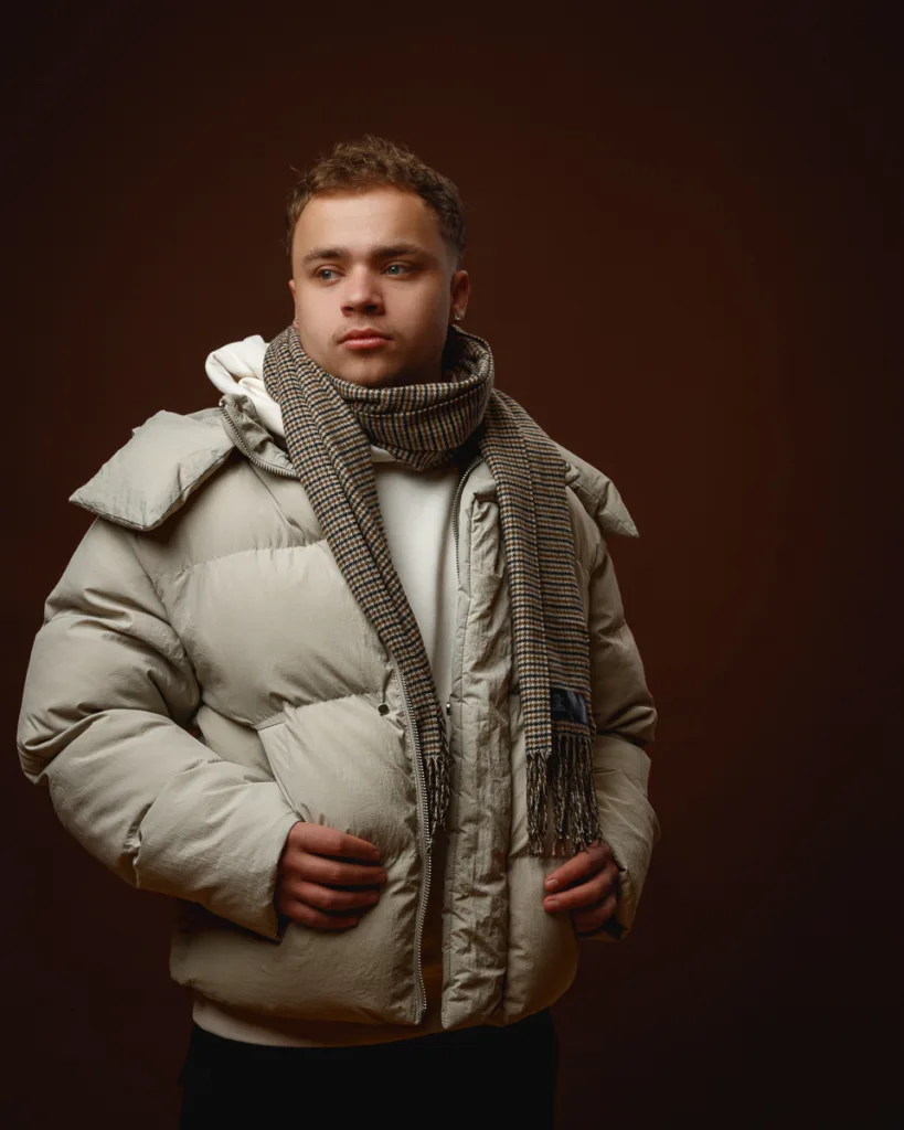 Man in puffer jacket and scarf, brown background.