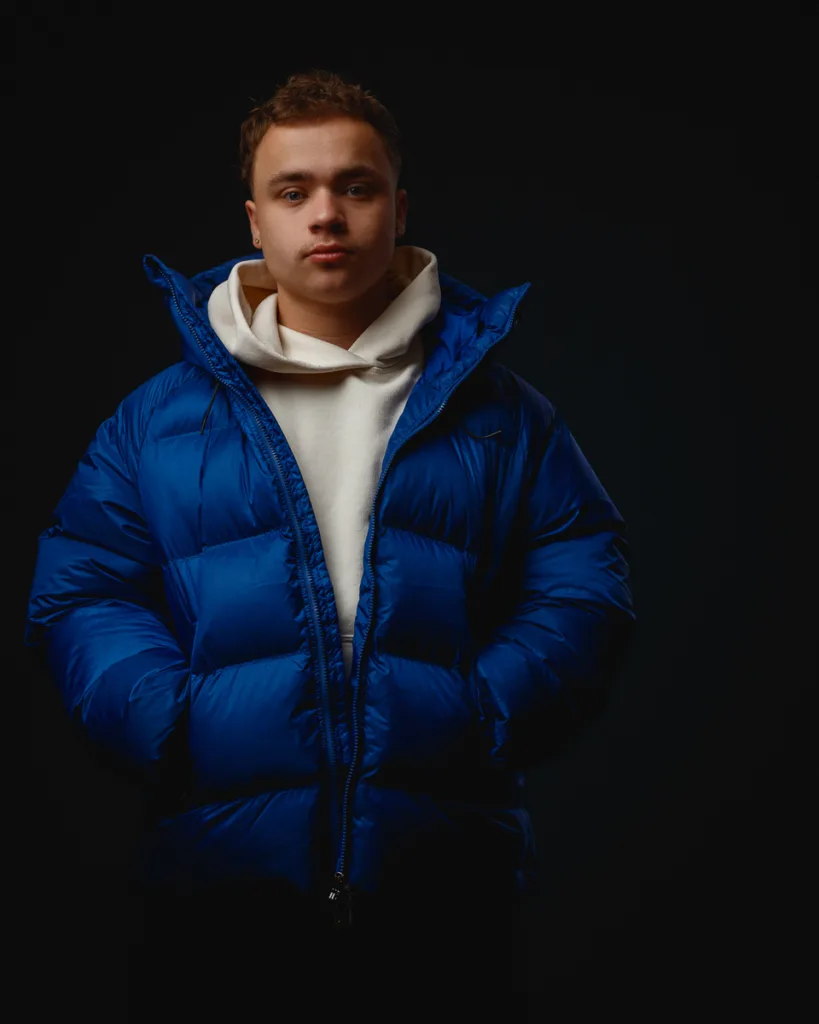 Person wearing blue jacket in dark studio setting.