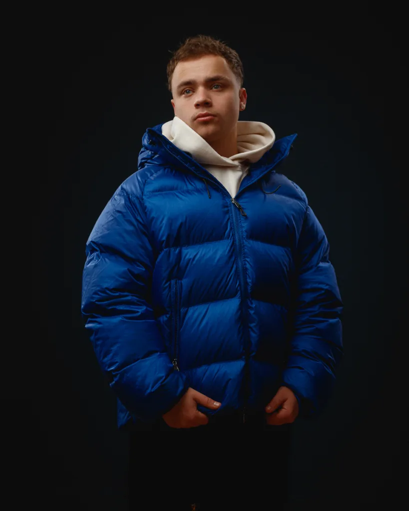 Person in blue puffer jacket against dark background.
