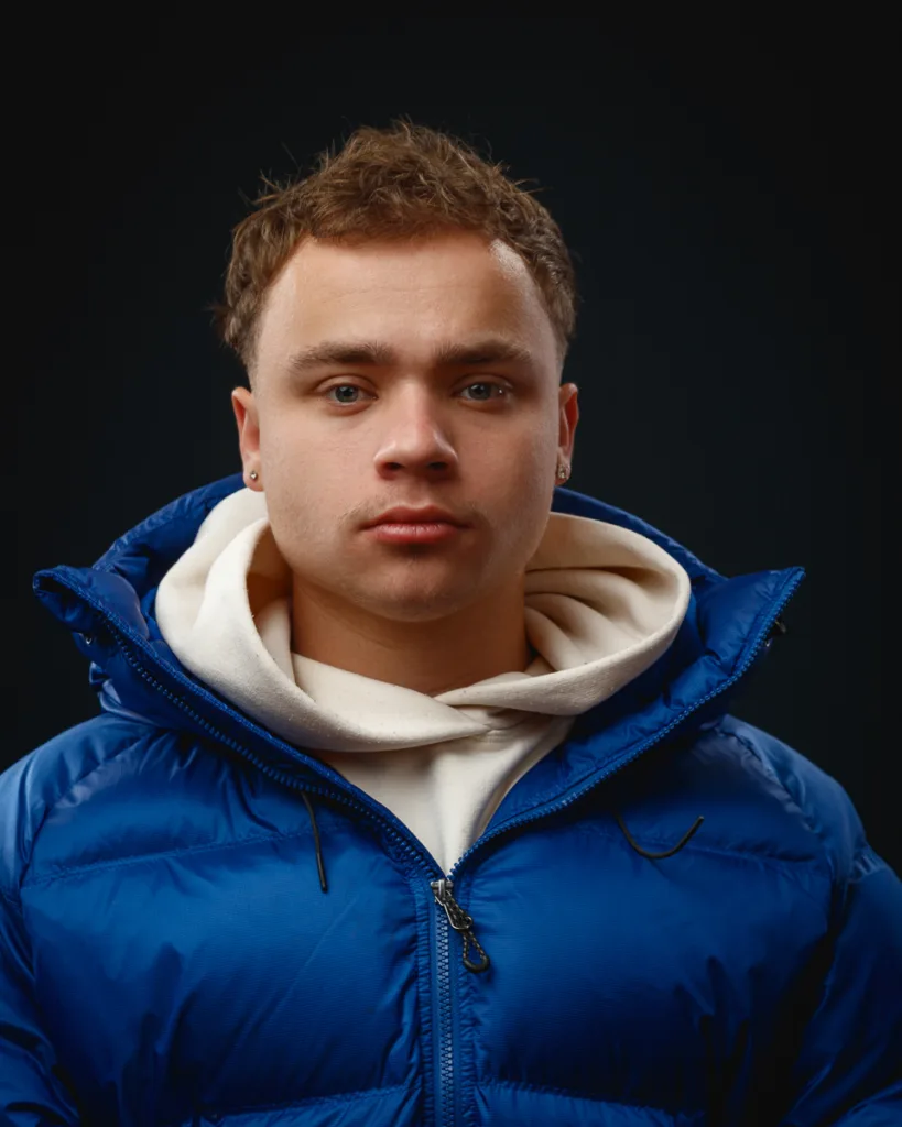 Person in blue jacket against dark background.