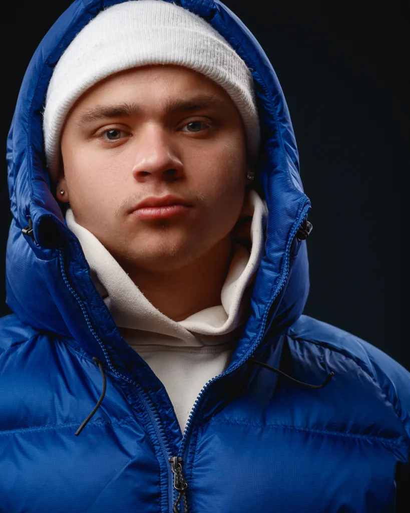 Person in blue jacket and white beanie, dark background.