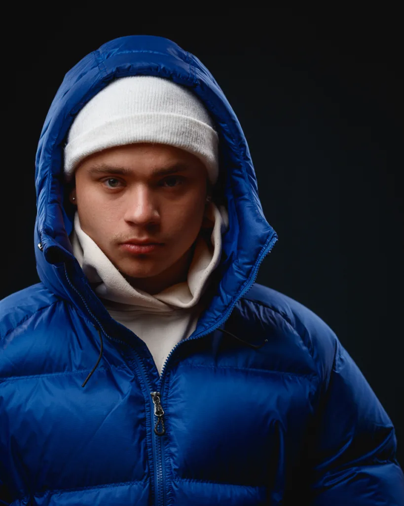 Person in blue jacket with white hat, dark background.