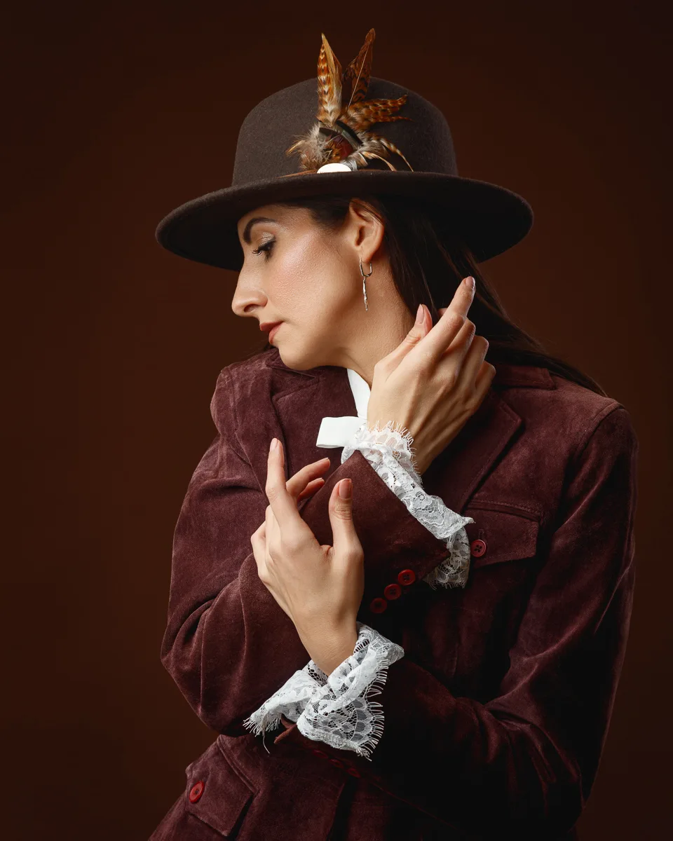 Studio portrait of a woman in a burgundy velvet jacket, lace cuffs and a feathered hat
