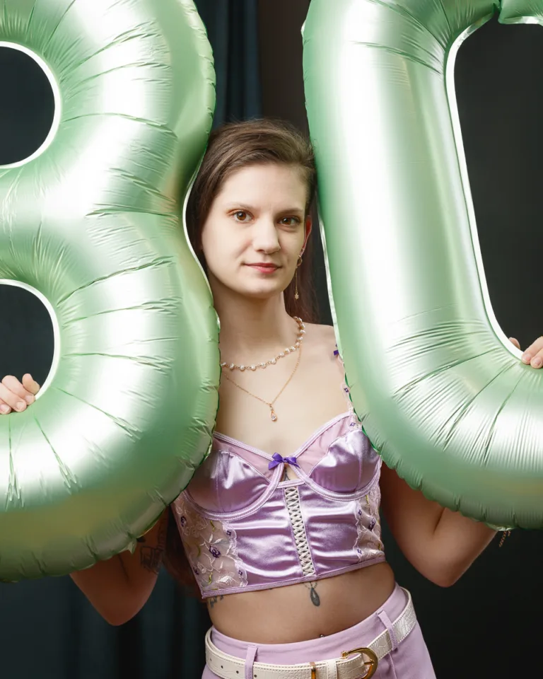 Woman holding large green balloons indoors.