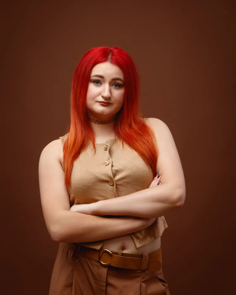 Person with red hair posing confidently against brown background