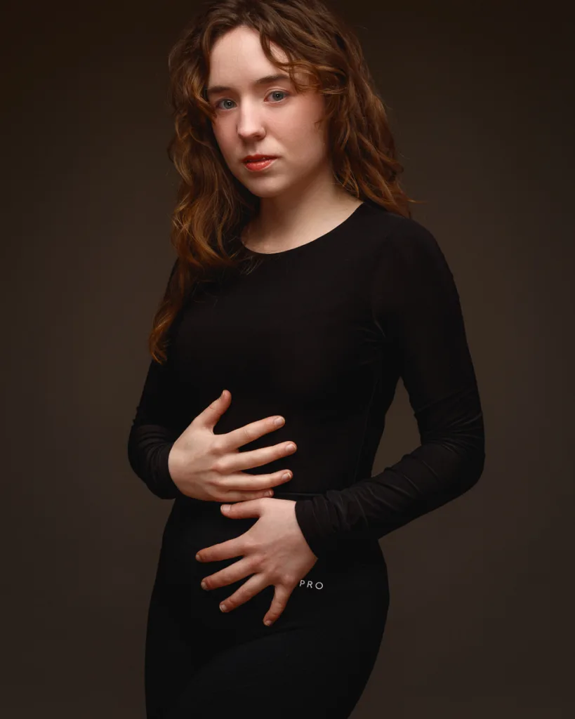 Person posing in black outfit against dark background