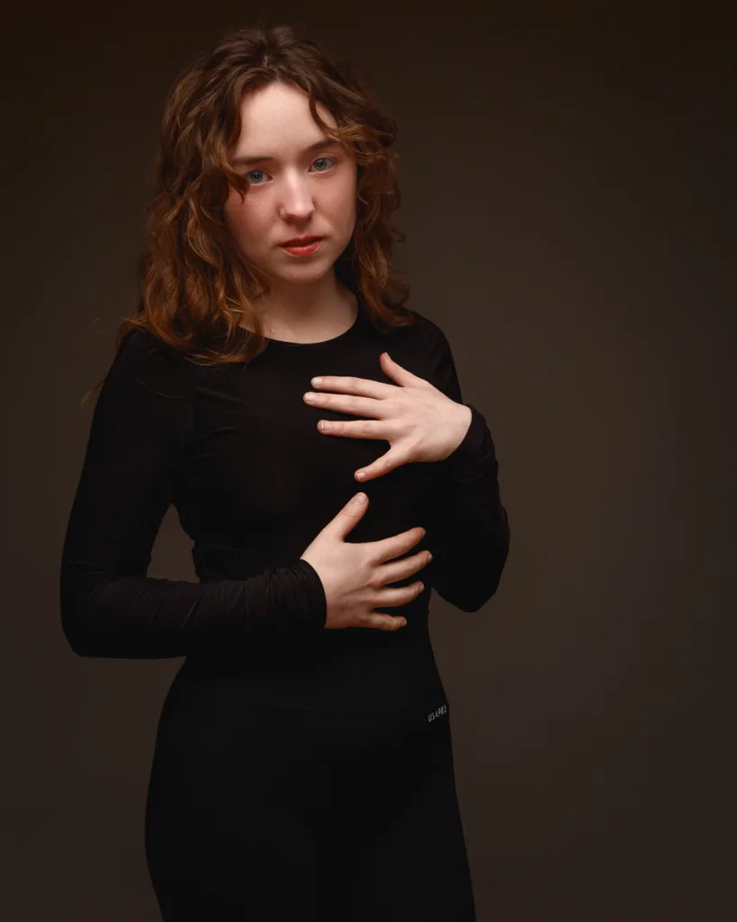 Person posing in black outfit on dark background