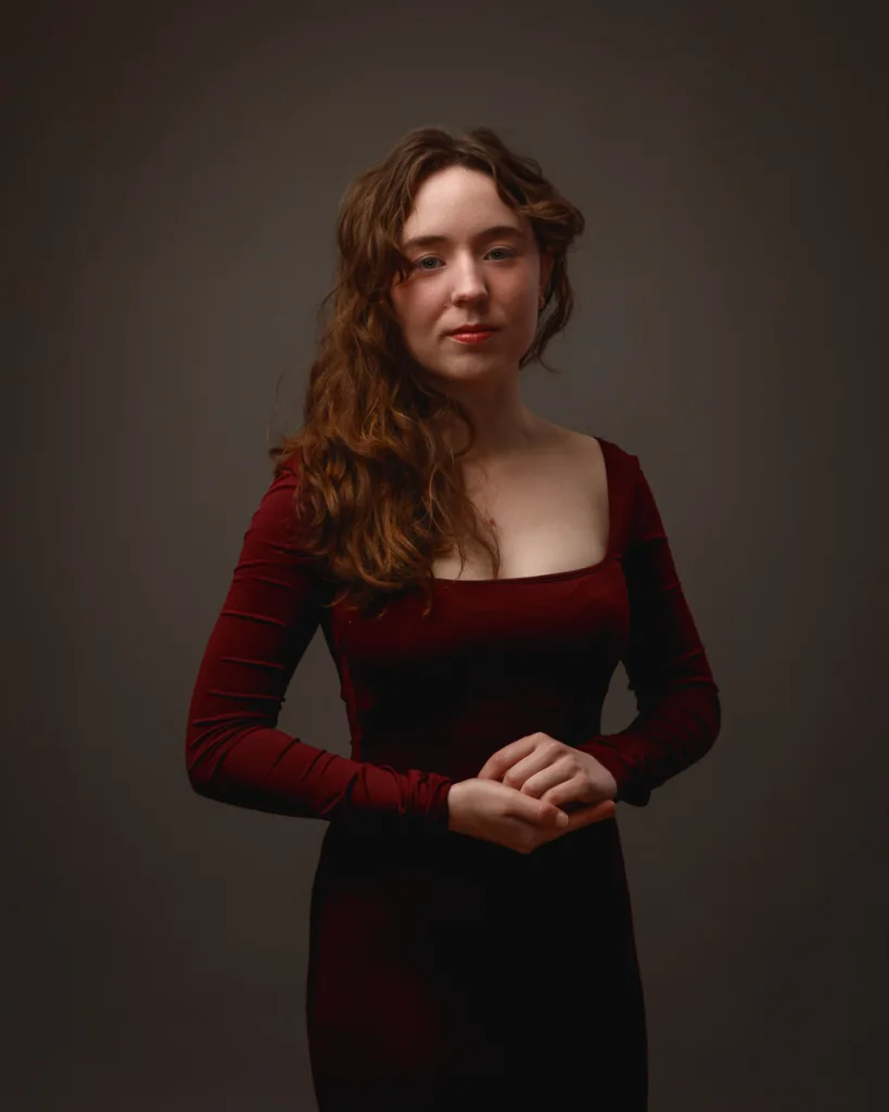Woman in burgundy dress posing against dark background