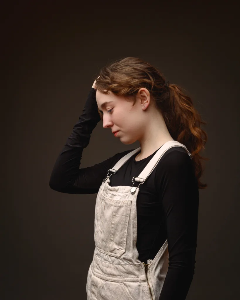 Person in overalls posing against dark background