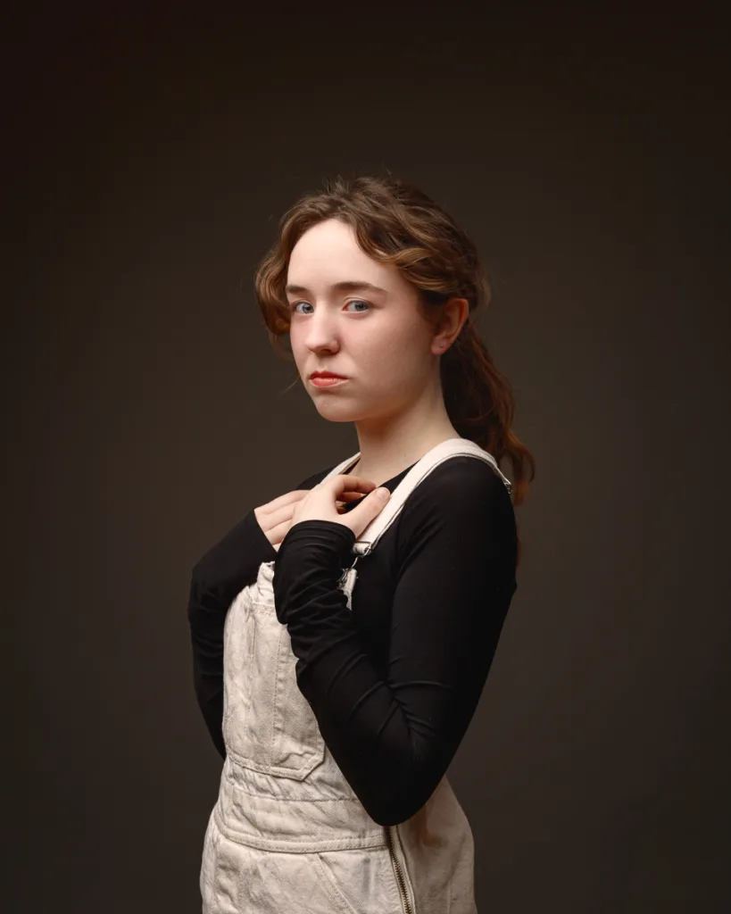 Person posing in studio wearing black top and overalls