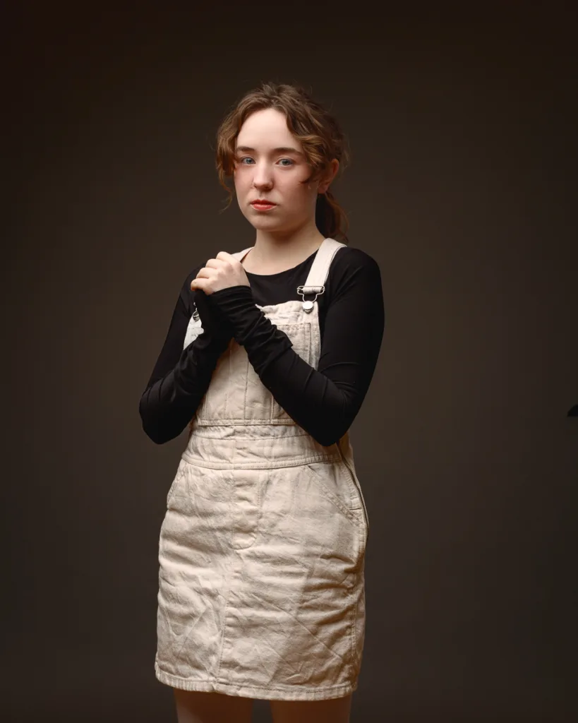 Young woman wearing beige pinafore poses indoors