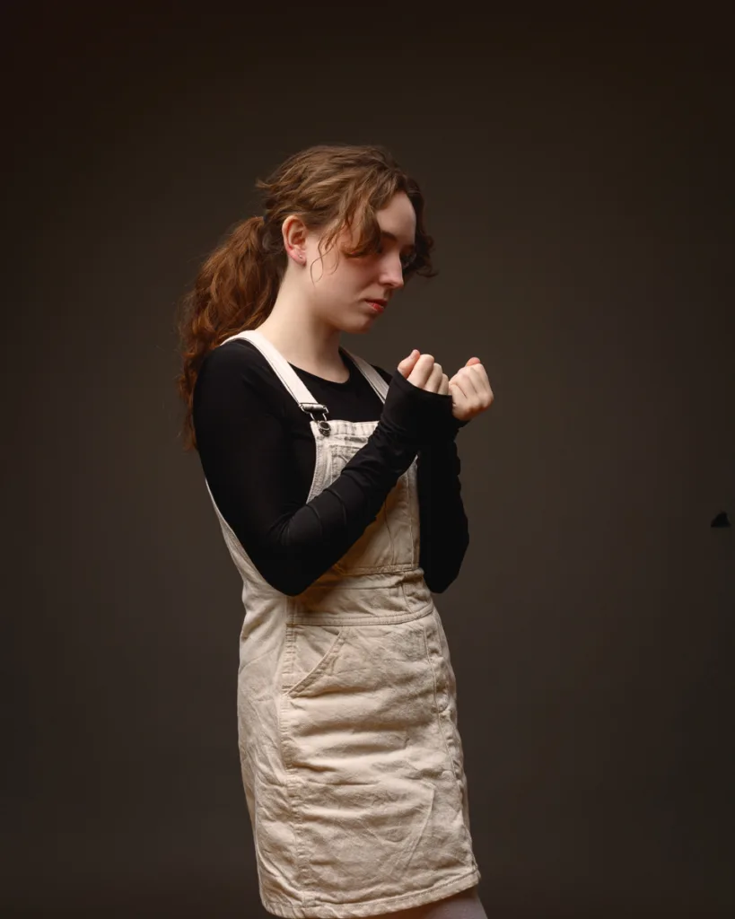 Woman in beige dungaree dress posing thoughtfully