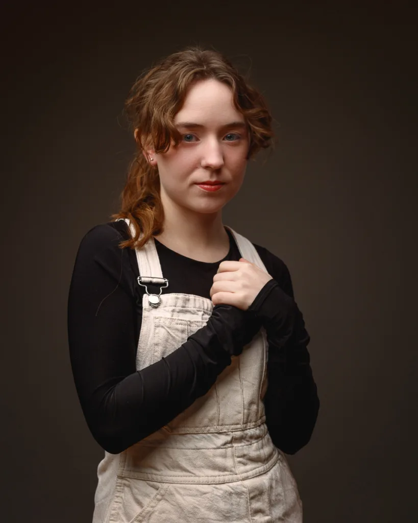 Person in dungarees posing against dark background